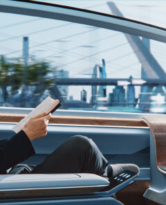 Futuristic Concept: Handsome Stylish Japanese Businessman in Glasses Reading Notebook and Watching News on Augmented Reality Screen while Sitting in a Autonomous Self-Driving Zero-Emissions Car.