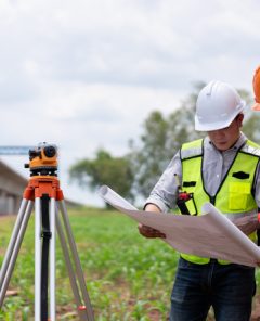 Surveyors and civil engineers using a theodolite and road construction plans to measure and inspect during the building process.