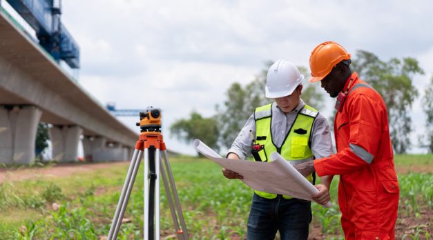 Surveyors and civil engineers using a theodolite and road construction plans to measure and inspect during the building process.