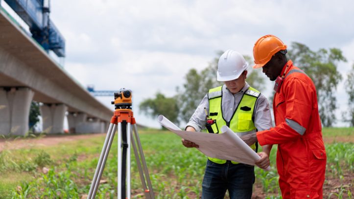 Surveyors and civil engineers using a theodolite and road construction plans to measure and inspect during the building process.